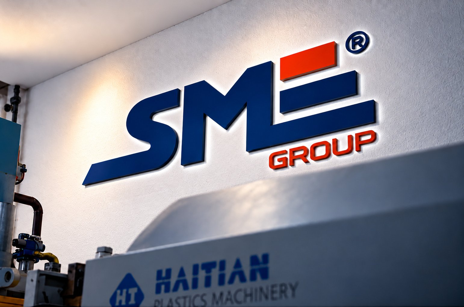 Letreiro SME Group aplicado na parede do galpão, acima de uma injetora Haitian